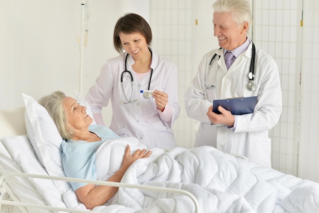 Portrait of happy senior woman in hospital with caring doctors
