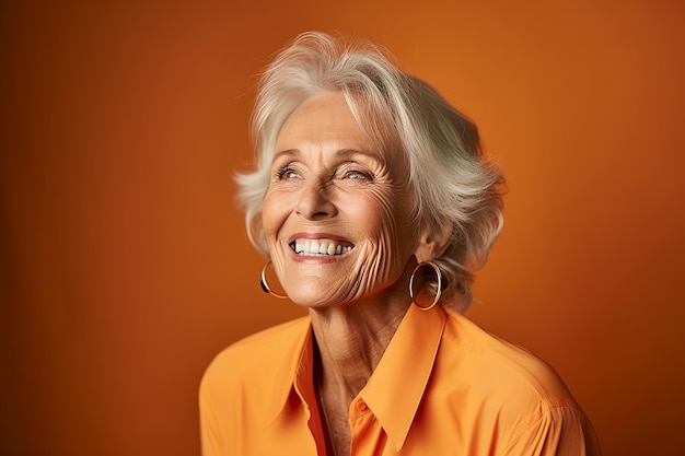 Portrait of a happy senior woman smiling at camera isolated over orange background