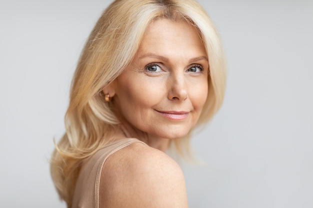 Portrait of happy senior woman with flawless skin and natural makeup posing on light background free