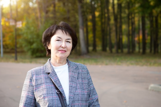 Portrait of a happy senora for 50 years in the park in autumn in a gray jacket.