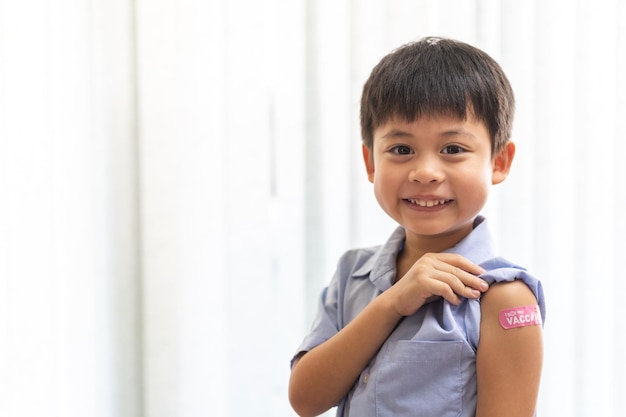 Портрет счастливой улыбки вакцинированного маленького азиатского мальчика в возрасте от 5 до 11 лет, позирующего с медицинской гипсовой повязкой после инъекционной вакцины Covid19 защита от коронавируса вакцинация ребенка