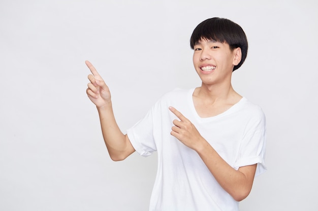 Portrait of a happy smiling Asian man wearing casual white t-shirt pointing hand to empty space beside on white background