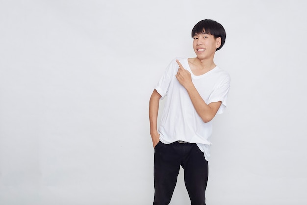 Photo portrait of a happy smiling asian man wearing casual white t-shirt pointing hand to empty space beside on white background