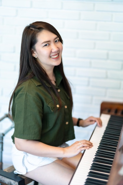 Ritratto felice sorridente bella donna asiatica che indossa un abito verde brunastro elegante hipster con suonare il vecchio pianoforte in legno stile classico vintage