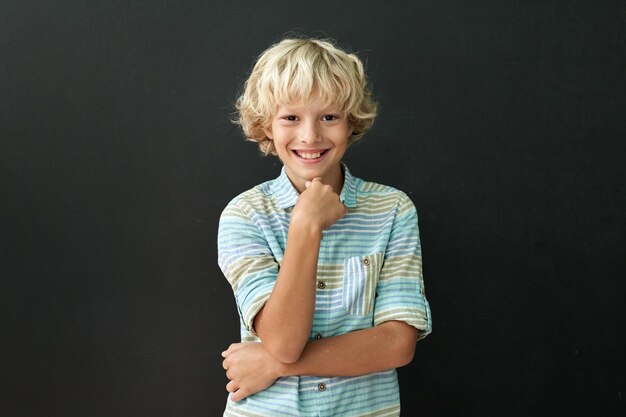 Photo portrait of happy smiling caucasian boy standing on chalkboard background