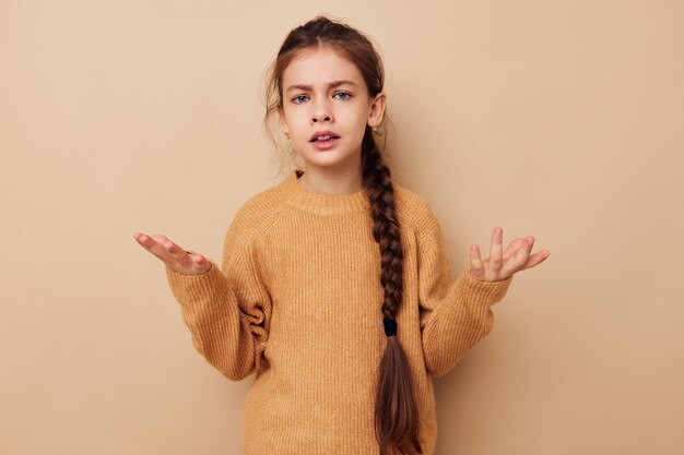 幸せな笑顔の子供の女の子の肖像ロングピグテールベージュセーターしかめっ面ベージュ背景