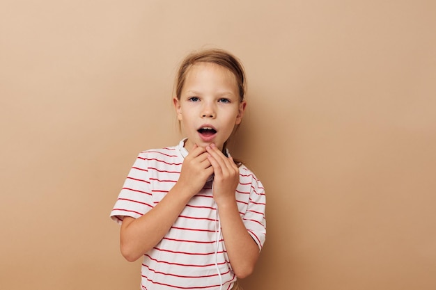 縞模様のTシャツヘッドフォンジェスチャーで幸せな笑顔の子供の女の子の肖像画は変更されていない子供時代を手にします