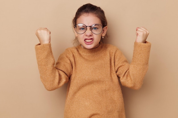 Portrait of happy smiling child girl with glasses emotions gesture hands beige background