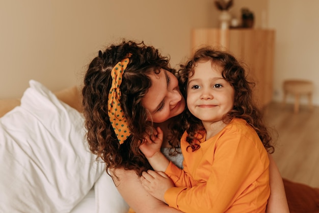Portrait of happy smiling curly-haired mom and daughter on mothers day at home
