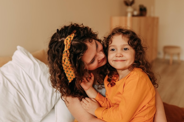 Foto ritratto di una madre e di una figlia dai capelli ricci e sorridenti il giorno della madre a casa