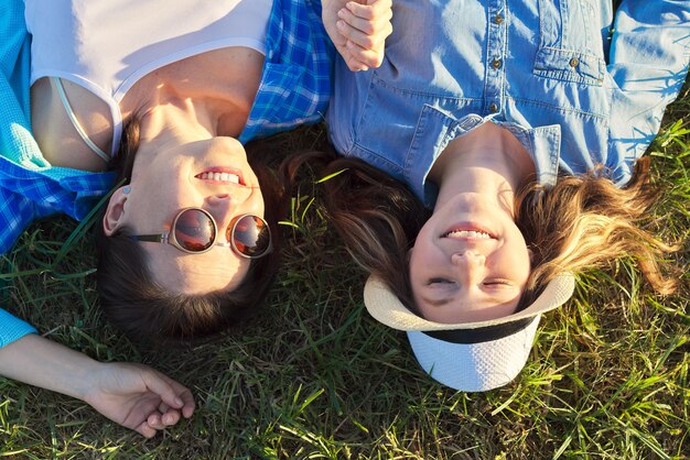 Portrait of happy smiling daughter and mother lying on the grass, top view. Mothers day, parent and teenage girl together in nature