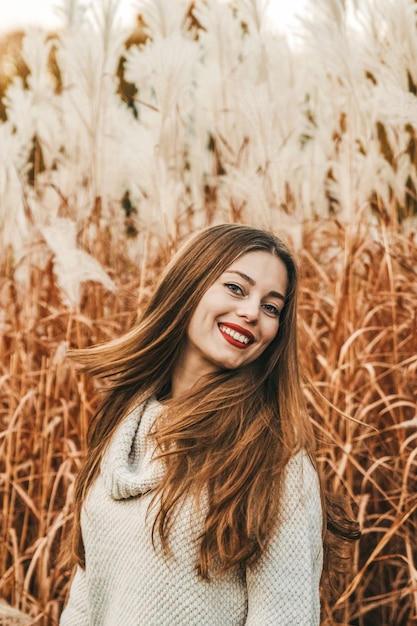 Портрет счастливой улыбающейся женщины осенью в поле. Она машет волосами.