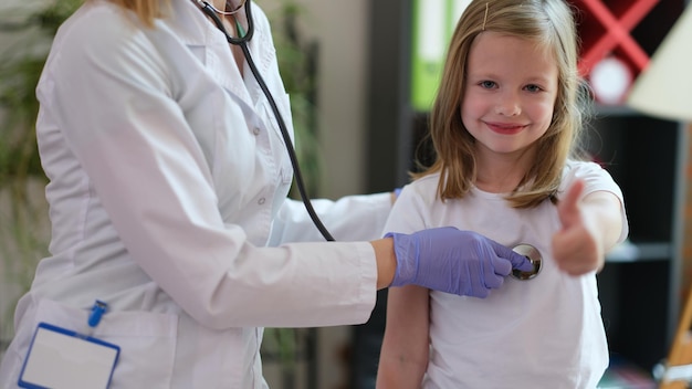 Portrait of happy smiling girl at doctor pediatrician appointment showing thumb up sigh