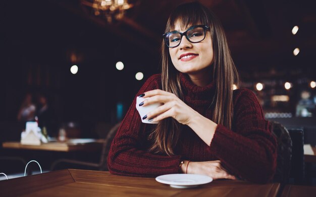 カップを保持している目の保護を提供するためのスタイリッシュな眼鏡で幸せな笑顔のヒップスターの女の子の肖像画