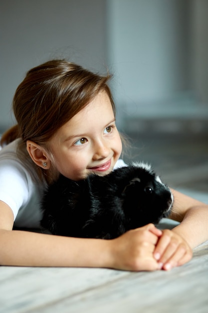 Ritratto di bambina sorridente felice che abbraccia cavia nera.