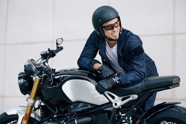 Portrait of happy smiling man in helmet leaning on motorcycle and looking away