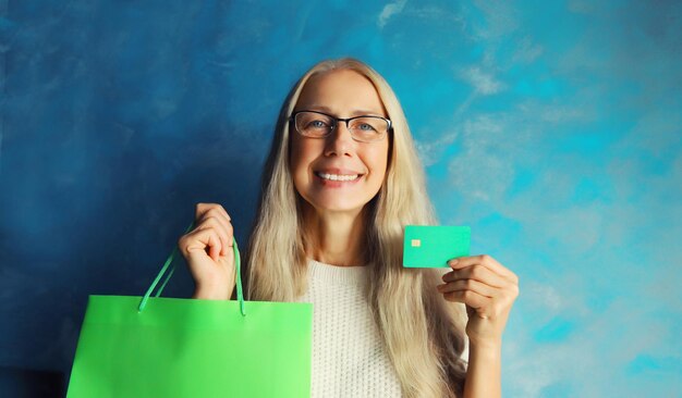 Portrait of happy smiling middle aged woman holding plastic credit bank card with shopping bags