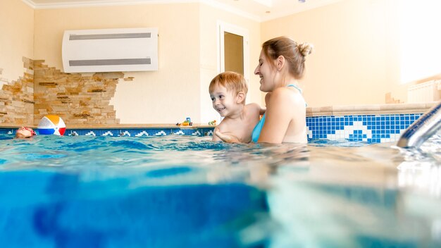 Portrait of happy smiling mother with 3 years old little son swimming in the pool at gym