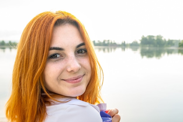 Foto ritratto di ragazza dai capelli rossi sorridente felice. giovane donna positiva che osserva nella macchina fotografica all'aperto.