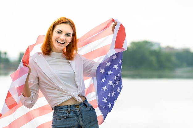 Portrait of happy smiling red haired girl with USA national flag on her shoulders. 