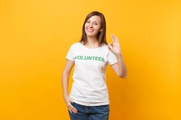 Portrait of happy smiling satisfied woman in white t-shirt with written inscription green title volunteer isolated on yellow background. Voluntary free assistance help, charity grace work concept.