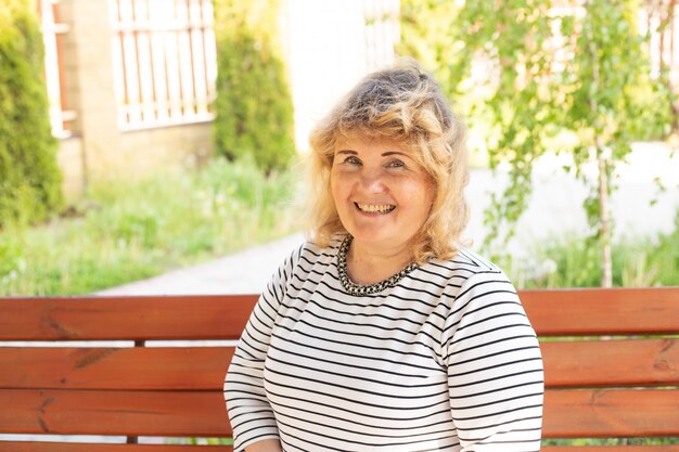 Portrait of happy smiling senior woman sitting on a bench on sunny day