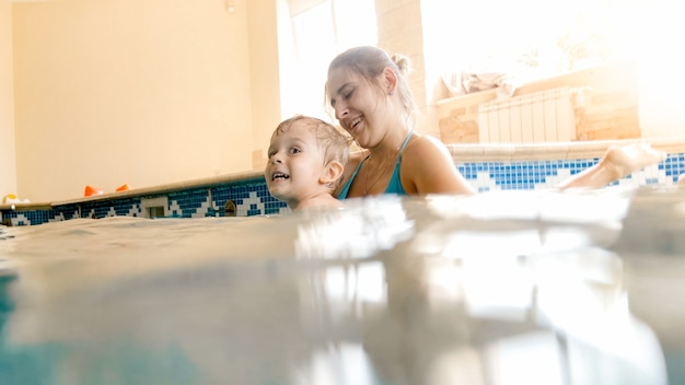 Portrait of happy smiling toddler boy learning swimming with mother in pool. Family having fun and relaxing in swimming pool