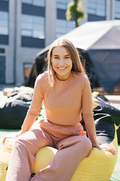 Ritratto di una donna sorridente felice seduta su un beanbag all'aperto in occhiali da sole in città