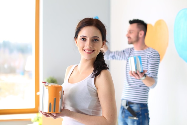 Portrait of happy smiling young couple painting interior wall of new house young couple