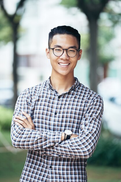 Portrait of happy smiling young man in glasses and plaid shirt crossing arms and looking at camera