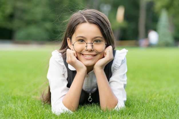 Portrait of happy teen girl in glasses lying on grass after school teen Teen girl