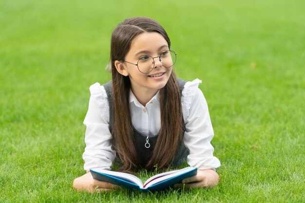 Portrait of happy teen girl reading school book lying on grass\
education school and education