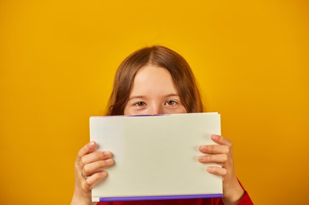 幸せな 10 代の女子高生の肖像画は本で彼女の顔をカバーします。