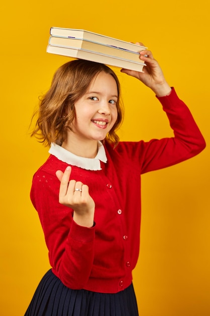 Ritratto di studentessa adolescente felice in uniforme che tiene libri sulla testa