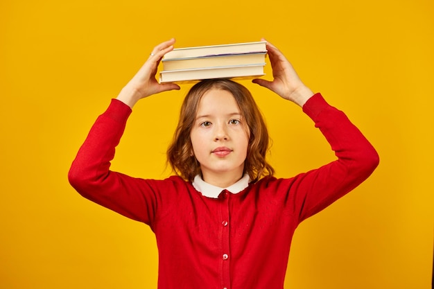 Portrait of happy teenage schoolgirl in uniform holding books on head