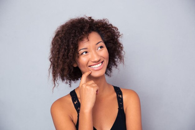 Portrait of happy thoughtful woman looking up over gray wall