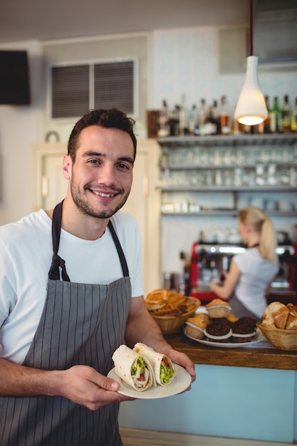 Portrait of happy waiter with fresh rolls at cafe