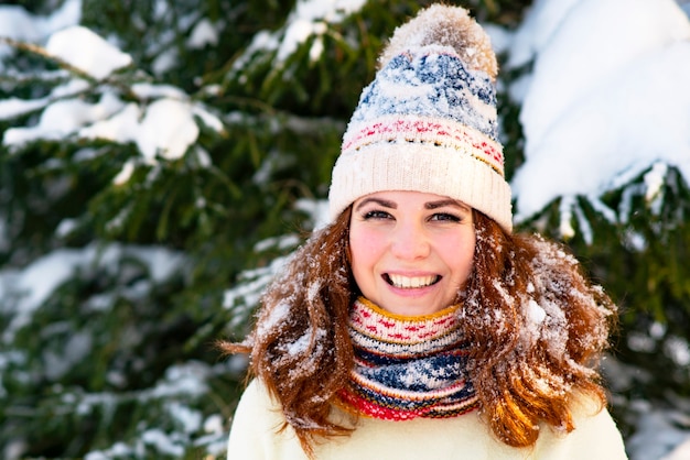 肖像画、雪を背景に幸せな女性、雪が女の子に降る、女性は屋外の外で、スカーフと帽子で冬に微笑む。