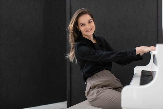 Ritratto di una donna felice in una camicia casual che suona il pianoforte a coda bianco su sfondo nero