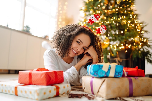 Портрет счастливой женщины, празднующей зимние праздники с большими подарочными коробками возле елки