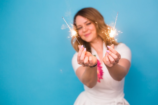 Portrait of a happy woman holding bengal lights over blue background with copy space. Christmas, celebrations and holidays concept