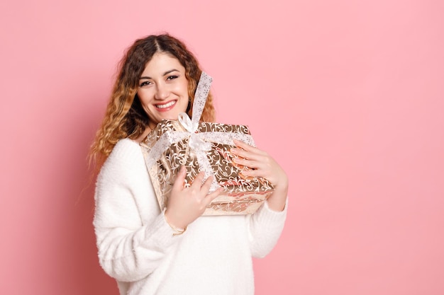 Portrait of a happy woman holding a gift box isolated on a pink background