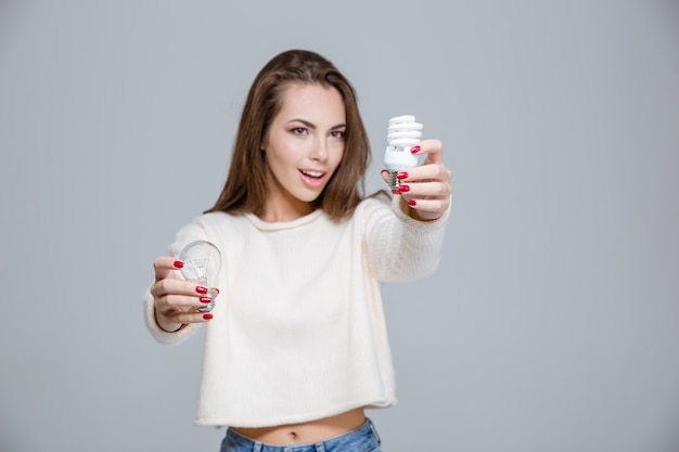 Portrait of a happy woman holding saving light bulb and normal light bulb over gray background