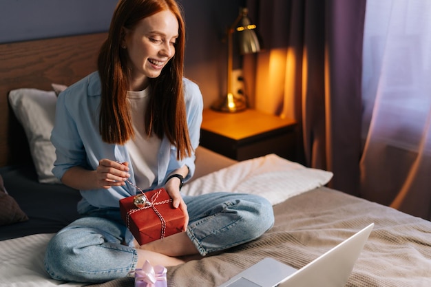 Portrait of happy woman opening gift box with present at cozy\
living room and looking on display