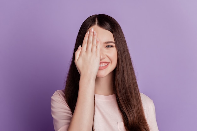紫色の背景に分離された幸せな女性の手のひらカバーアイウォッチ歯を見せる笑顔の肖像画