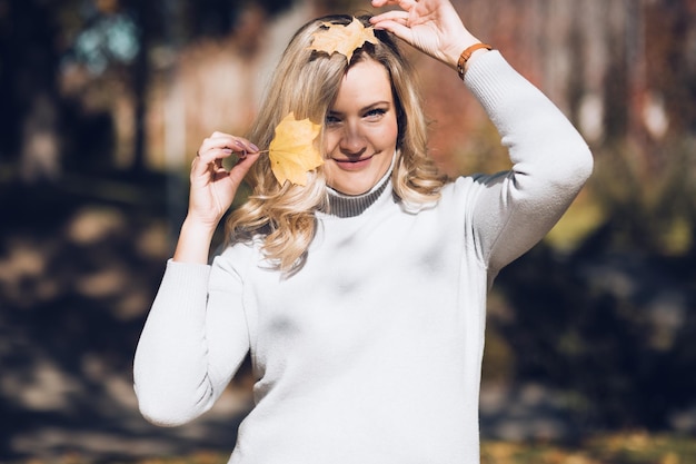 Portrait of happy woman playing with fallen foliage in autumn city park on sunny day closeup adult l