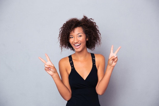 Portrait of a happy woman showing victory with fingers over gray wall and looking at front