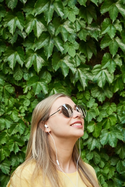 Portrait of a happy woman in sunglasses uses headphones to listen to music audio summer time