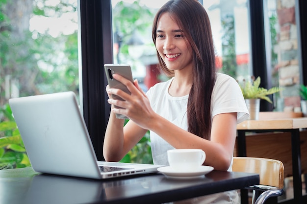 Portrait of a happy woman using a smart phone and a laptop sitting in a table