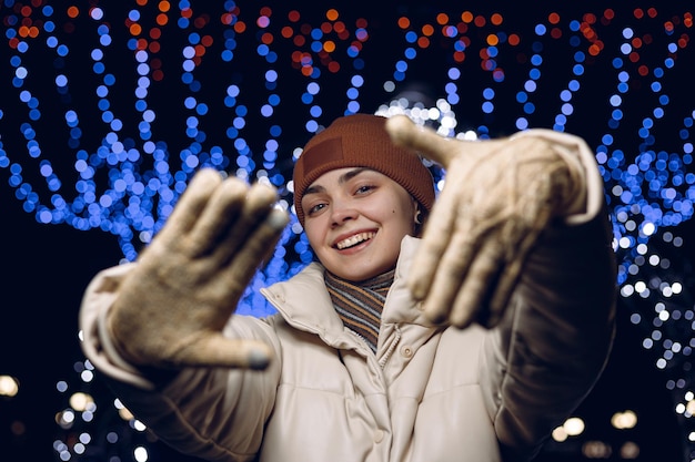 Photo portrait of happy woman in warm clothes showing frame gesture and looking at camera